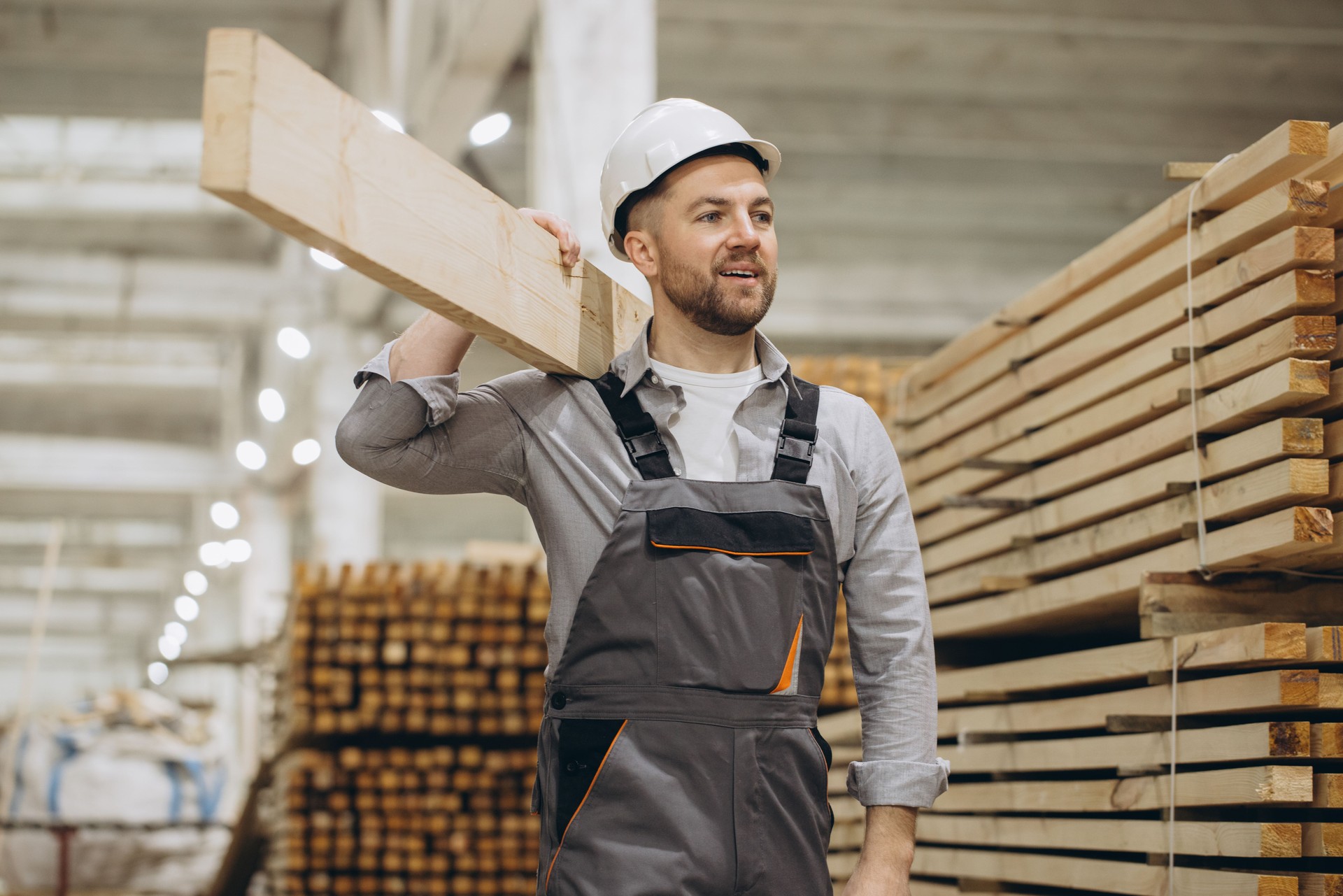 Carpenter carrying wooden plank in lumber warehouse